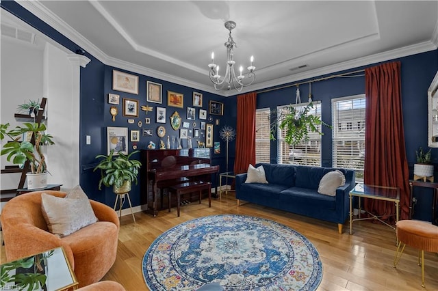 living area featuring a notable chandelier, wood finished floors, visible vents, a raised ceiling, and ornate columns