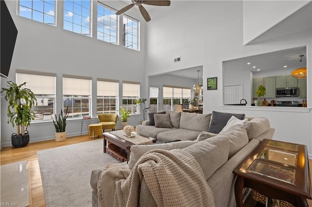 living room featuring ceiling fan, wood finished floors, visible vents, and baseboards