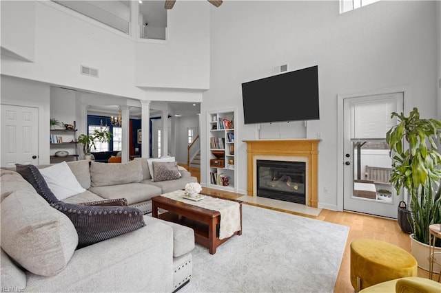 living room with ceiling fan with notable chandelier, a fireplace with flush hearth, wood finished floors, visible vents, and stairs