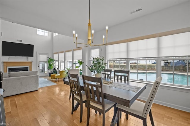 dining room with light wood-style flooring, a fireplace, visible vents, and a notable chandelier