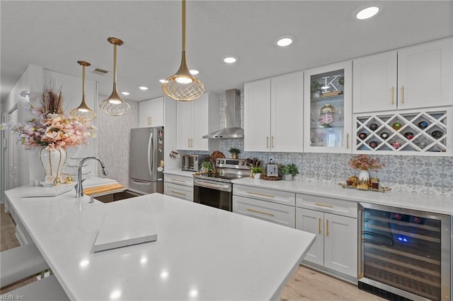 kitchen with wall chimney range hood, beverage cooler, appliances with stainless steel finishes, white cabinets, and a sink