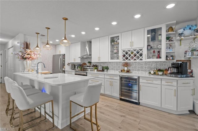 kitchen with light wood-type flooring, a breakfast bar, stainless steel appliances, wine cooler, and wall chimney exhaust hood