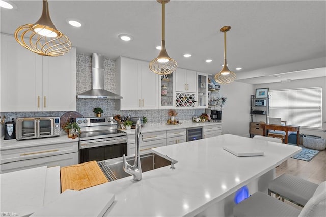 kitchen featuring stainless steel electric range oven, a breakfast bar area, decorative backsplash, wine cooler, and wall chimney exhaust hood