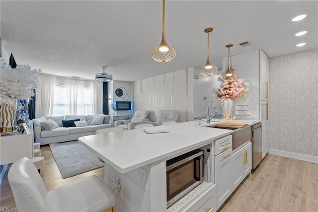 kitchen with visible vents, light wood finished floors, wallpapered walls, a peninsula, and stainless steel appliances