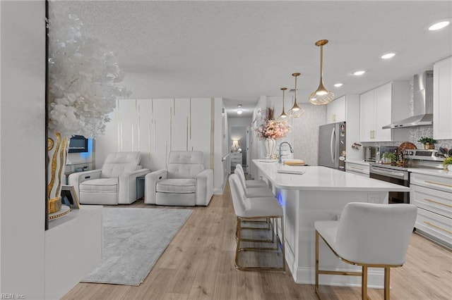 kitchen featuring wall chimney range hood, light wood-type flooring, a kitchen bar, stainless steel appliances, and a sink