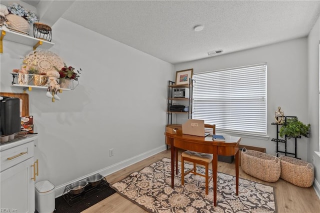 office with light wood-type flooring, visible vents, baseboards, and a textured ceiling