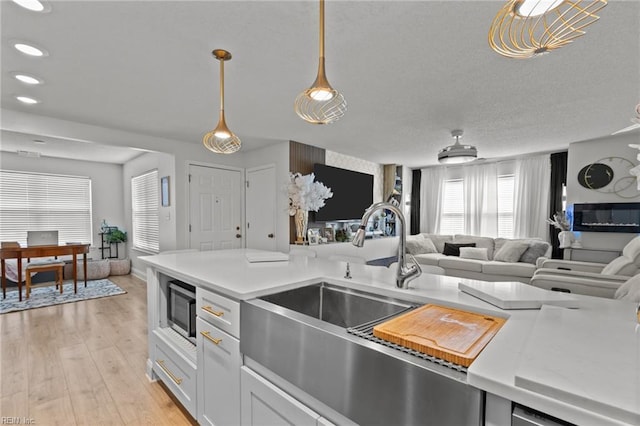 kitchen featuring stainless steel microwave, open floor plan, light countertops, light wood-style floors, and a sink