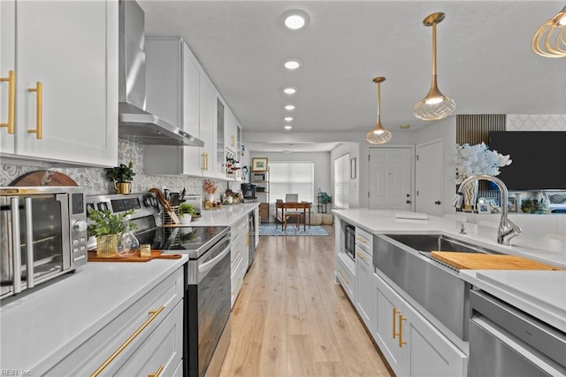 kitchen with wall chimney range hood, light countertops, light wood-style flooring, white cabinets, and stainless steel appliances