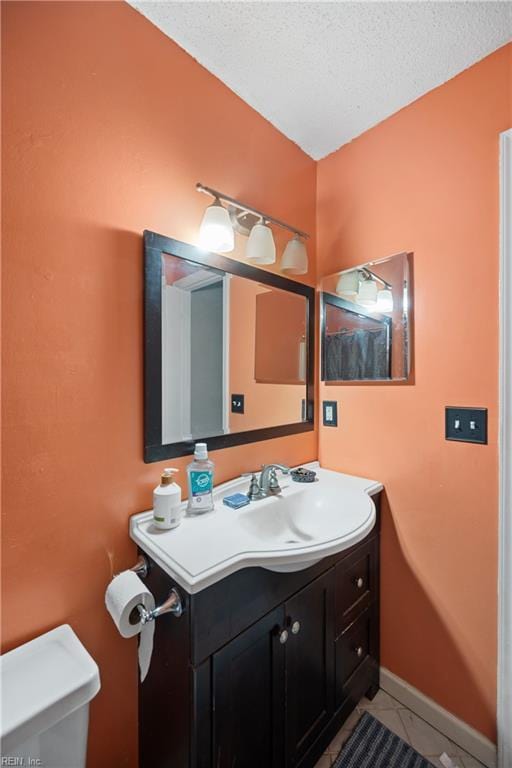 half bathroom featuring baseboards, toilet, tile patterned flooring, a textured ceiling, and vanity