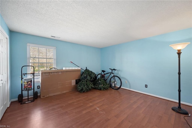 interior space featuring visible vents, a textured ceiling, baseboards, and wood finished floors