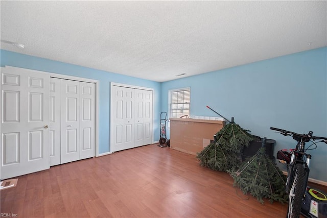 bedroom featuring two closets, visible vents, a textured ceiling, wood finished floors, and baseboards