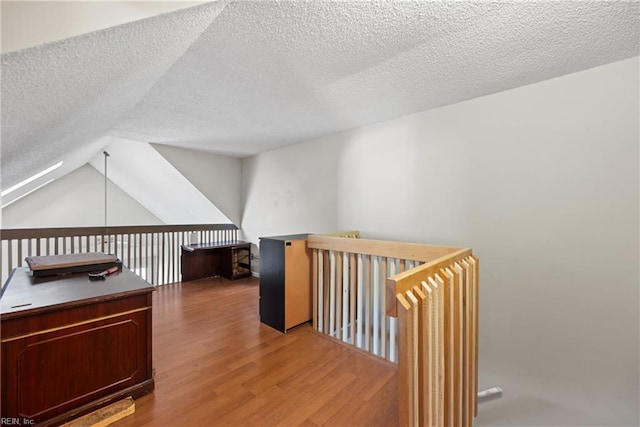 additional living space featuring vaulted ceiling, a textured ceiling, and wood finished floors