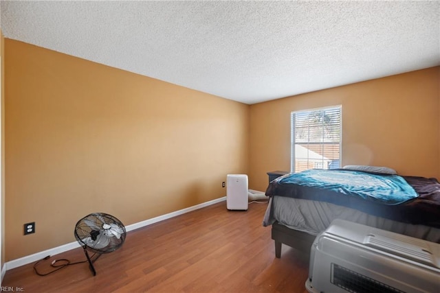 bedroom with light wood-style floors, baseboards, and a textured ceiling