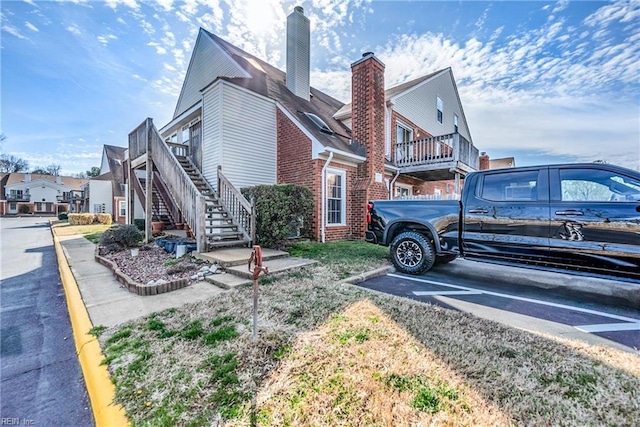 view of home's exterior with uncovered parking, brick siding, stairway, and a chimney