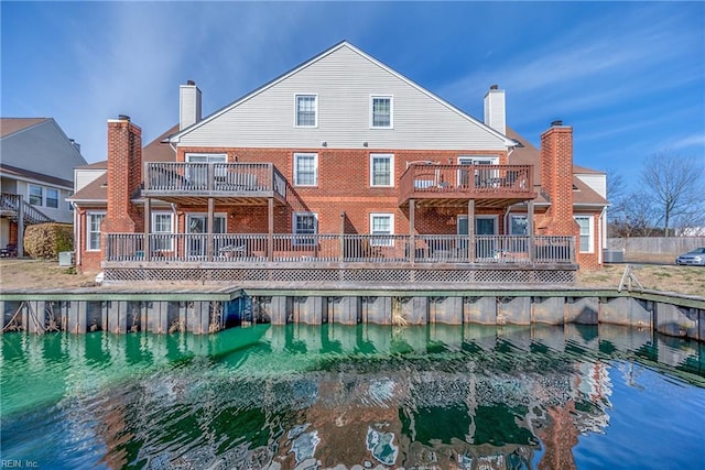 back of property with a water view, a chimney, and brick siding