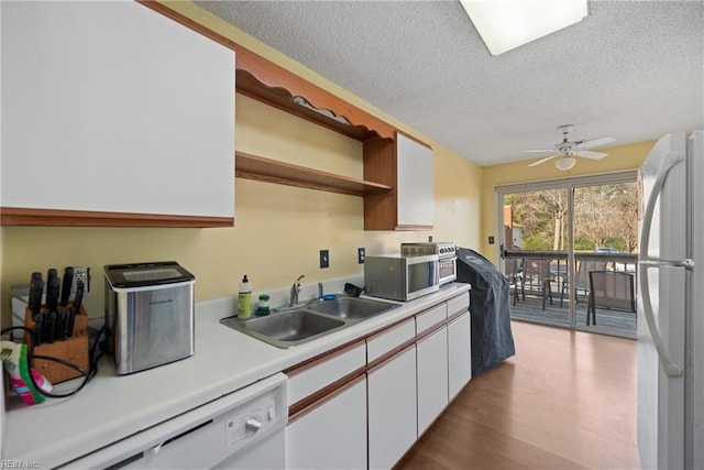 kitchen with white appliances, wood finished floors, a sink, white cabinetry, and light countertops