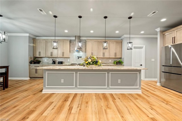 kitchen with wall chimney range hood, visible vents, ornamental molding, and freestanding refrigerator