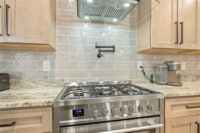 kitchen featuring stainless steel gas range oven, wall chimney range hood, light stone counters, and tasteful backsplash