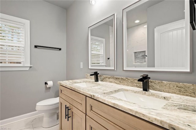 bathroom with marble finish floor, double vanity, a sink, and toilet