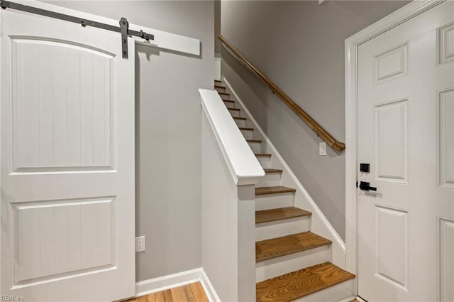 staircase with a barn door, wood finished floors, and baseboards