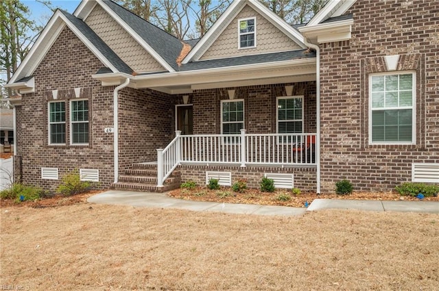 view of front facade featuring a porch, crawl space, brick siding, and roof with shingles