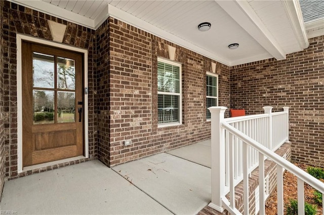 view of exterior entry with a porch and brick siding