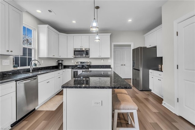 kitchen with a center island, stainless steel appliances, a kitchen bar, white cabinetry, and a sink