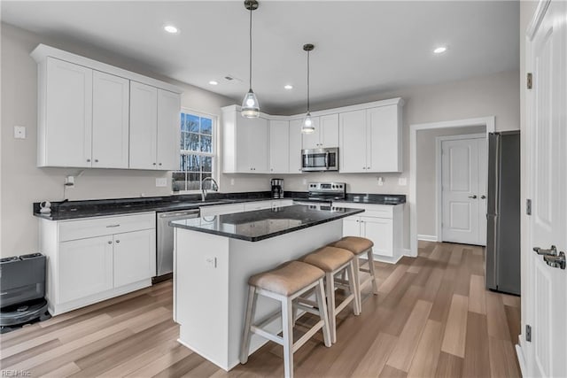 kitchen with stainless steel appliances, light wood-style floors, a kitchen bar, and white cabinets