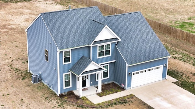 view of front facade featuring driveway, a shingled roof, central AC unit, an attached garage, and fence