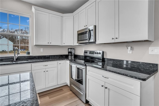 kitchen featuring a sink, white cabinets, light wood-style floors, appliances with stainless steel finishes, and dark stone countertops