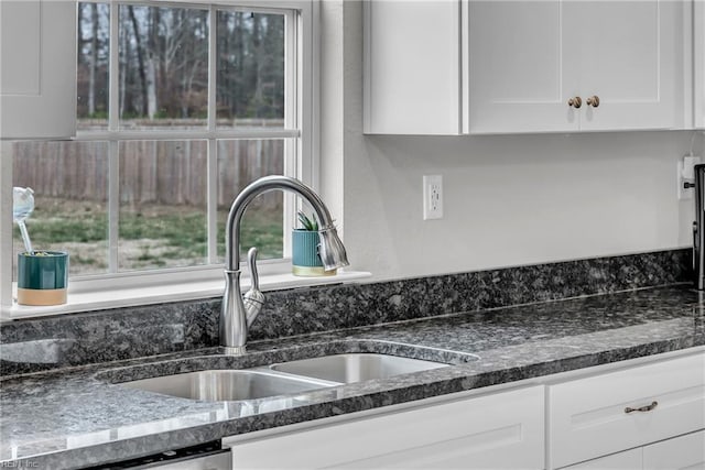 details with dishwashing machine, dark stone countertops, white cabinets, and a sink