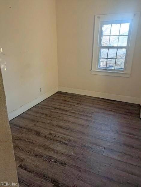 spare room featuring dark wood-type flooring and baseboards