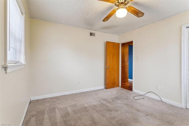 empty room with a textured ceiling, carpet flooring, a ceiling fan, visible vents, and baseboards