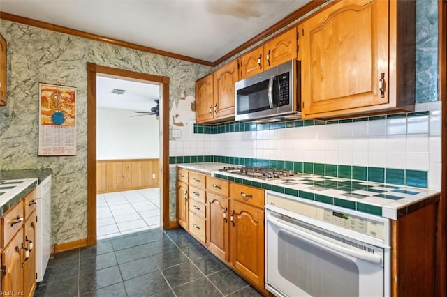 kitchen with a wainscoted wall, tile countertops, a ceiling fan, white appliances, and wallpapered walls