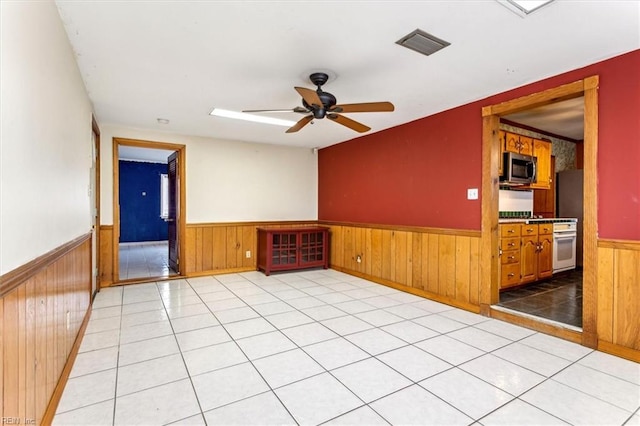 unfurnished room with a wainscoted wall, ceiling fan, wood walls, and visible vents