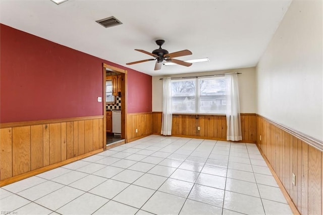 empty room featuring wooden walls, wainscoting, visible vents, and a ceiling fan