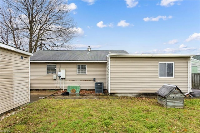 rear view of house with central AC unit and a lawn