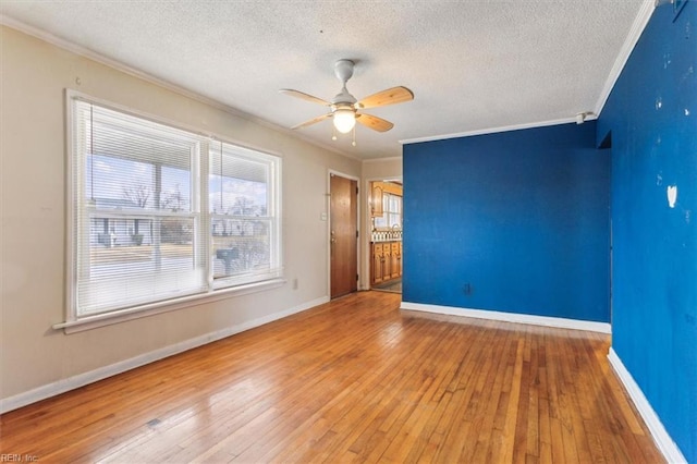 empty room featuring ornamental molding, wood-type flooring, baseboards, and a ceiling fan