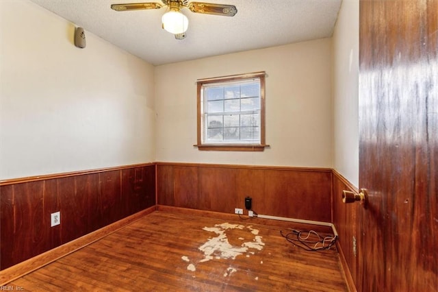 unfurnished room featuring a wainscoted wall, a textured ceiling, a ceiling fan, and wood finished floors