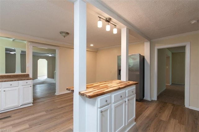 kitchen featuring butcher block counters, arched walkways, white cabinets, and light wood-style flooring