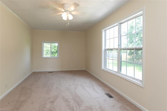 empty room featuring plenty of natural light, visible vents, crown molding, and carpet flooring