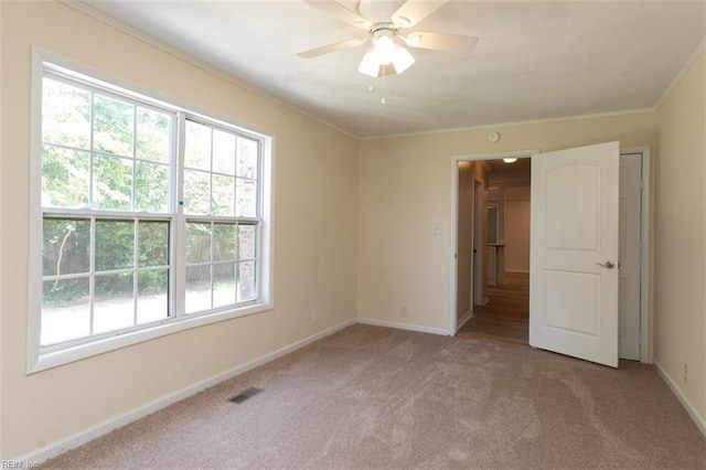 empty room featuring visible vents, ornamental molding, a ceiling fan, carpet flooring, and baseboards