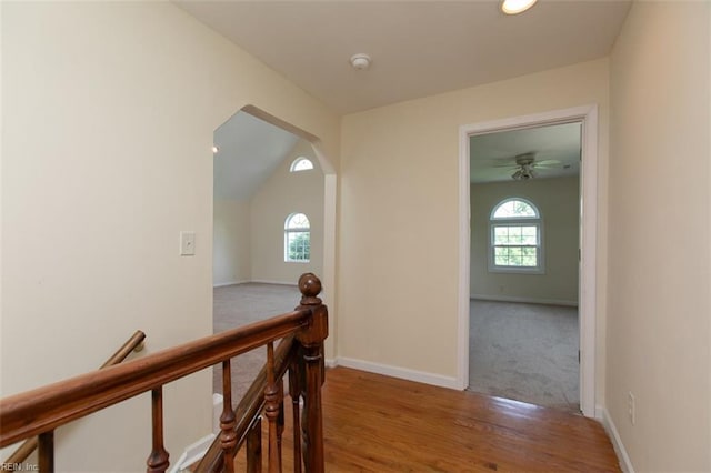 hall featuring arched walkways, wood finished floors, an upstairs landing, and baseboards