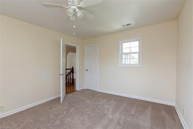 carpeted empty room with baseboards, visible vents, and a ceiling fan