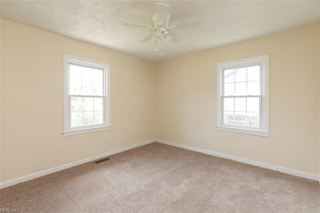 carpeted spare room featuring baseboards, visible vents, ceiling fan, and a wealth of natural light