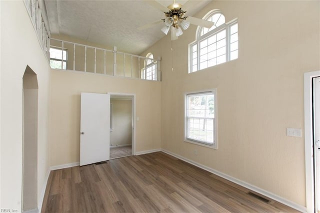 empty room featuring ceiling fan, wood finished floors, a towering ceiling, visible vents, and baseboards