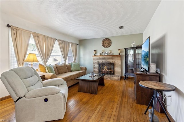 living area featuring hardwood / wood-style flooring, a brick fireplace, and a textured ceiling