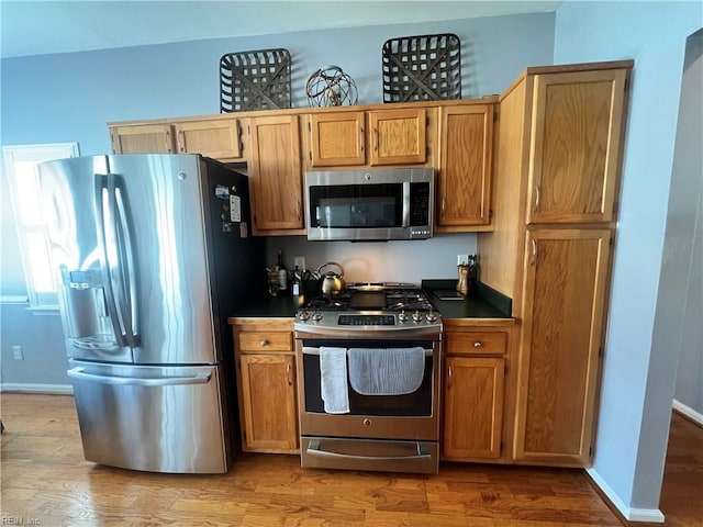 kitchen featuring wood finished floors, baseboards, stainless steel appliances, dark countertops, and brown cabinets