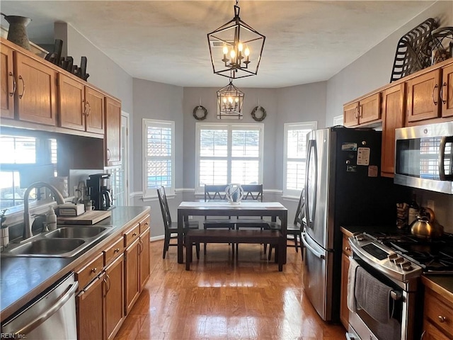 kitchen with an inviting chandelier, light wood-style flooring, a sink, stainless steel appliances, and decorative light fixtures