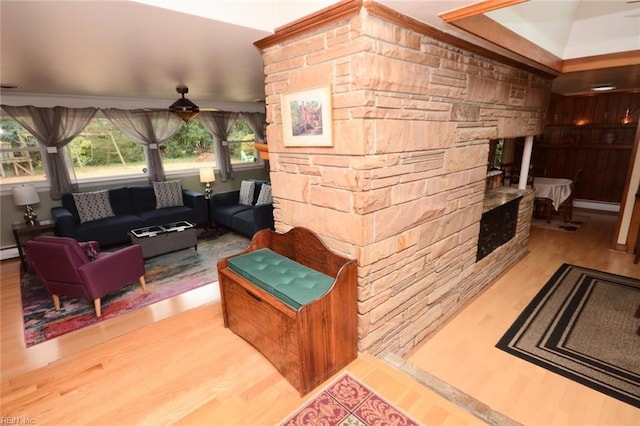 living area with a stone fireplace, a baseboard radiator, and wood finished floors